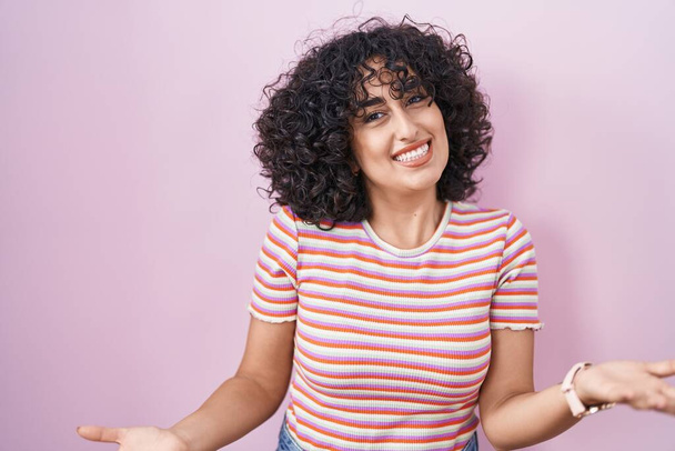 Nuori Lähi-idän nainen seisoo vaaleanpunainen tausta hymyilevä iloinen avosylin ystävällinen tervetullut, positiivinen ja luottavainen tervehdys  - Valokuva, kuva
