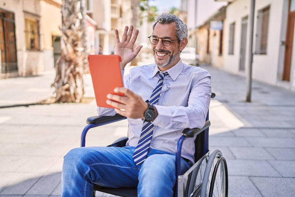 Uomo ispanico di mezza età seduto sulla sedia a rotelle con videochiamata in strada - Foto, immagini