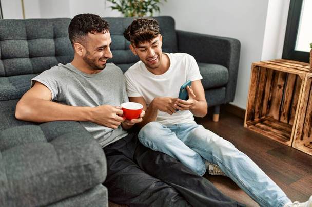 Due uomini ispanici coppia utilizzando smartphone e bere caffè a casa - Foto, immagini