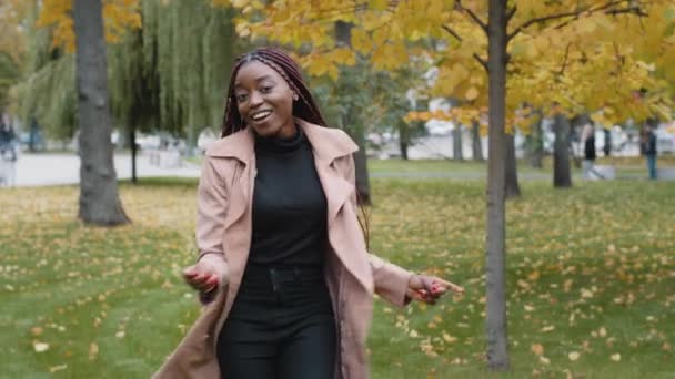Active energetic positive joyful woman dancing in autumn park having fun young attractive satisfied african girl moves to music outdoors performing funny dance rejoices in success good mood concept - Filmagem, Vídeo