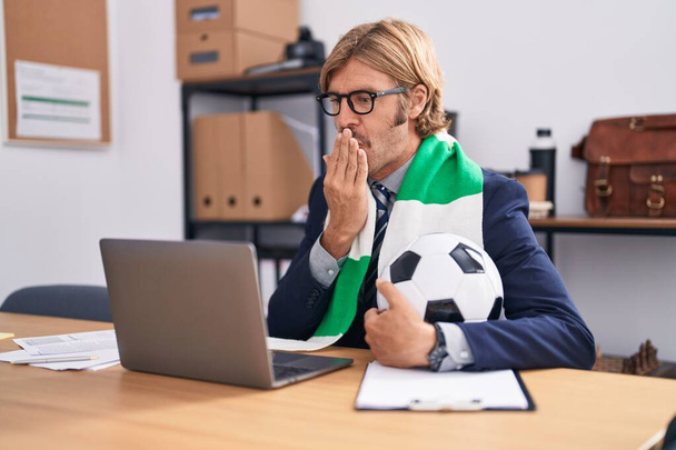 Καυκάσιος με μουστάκι που δουλεύει στο γραφείο υποστηρίζοντας ποδοσφαιρική ομάδα που καλύπτει το στόμα με το χέρι, σοκαρισμένος και φοβισμένος για λάθος. έκπληκτη έκφραση  - Φωτογραφία, εικόνα