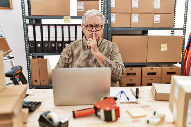 Senior caucasian man working at small business ecommerce with laptop asking to be quiet with finger on lips. silence and secret concept.  - Photo, image