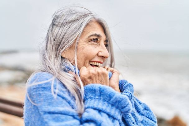 Седовласая женщина средних лет, уверенно улыбающаяся, глядя в сторону моря - Фото, изображение