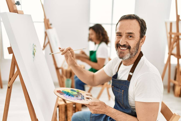 Dos estudiantes de mediana edad sonriendo feliz pintura en el estudio de arte. - Foto, imagen