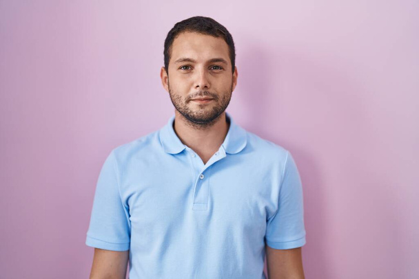 Hispanic man standing over pink background relaxed with serious expression on face. simple and natural looking at the camera.  - Photo, image