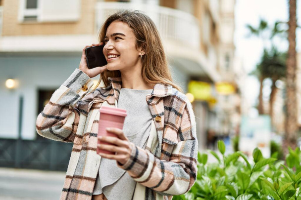 Nuori blondi nainen, jolla on kahvia puhumassa älypuhelimella kadulla - Valokuva, kuva