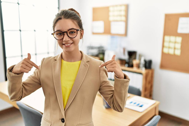 Young brunette teenager wearing business style at office looking confident with smile on face, pointing oneself with fingers proud and happy.  - Zdjęcie, obraz