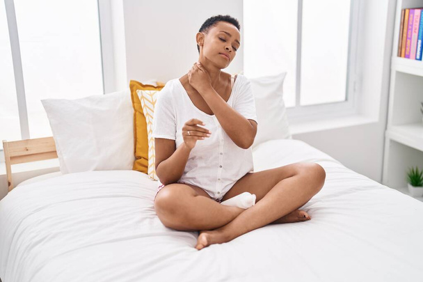 African american woman applying skin treatment sitting on bed at bedroom - Photo, Image