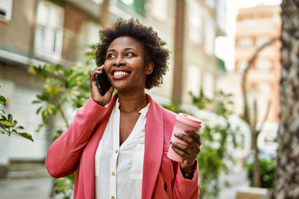 Beautiful business african american woman with afro hair smiling happy and confident outdoors at the city having a conversation speaking on the phone - 写真・画像