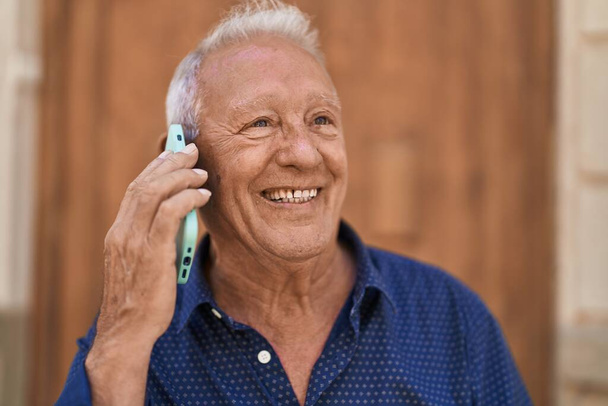 Senior grey-haired man smiling confident talking on the smartphone at street - 写真・画像