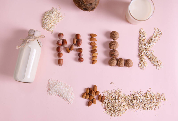 Flat lay Lettering Milk on pink background, using wholesome ingredients, cereals, nuts and seeds. Bottle of vegetable, alternative, dairy free milk made from White Rice Oatmeal sesame Almonds Coconut - Foto, afbeelding