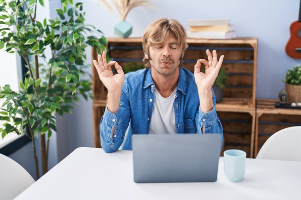 Fiatal férfi használ laptop csinál jóga gyakorlatok otthon - Fotó, kép