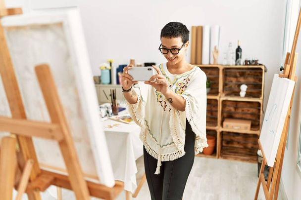 Νεαρή ισπανόφωνη γυναίκα κάνει φωτογραφία από το smartphone για να ζωγραφίσει σε στούντιο τέχνης - Φωτογραφία, εικόνα