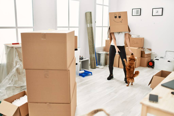 Young hispanic woman wearing funny cardboard on head playing with dogs at new home - Photo, Image