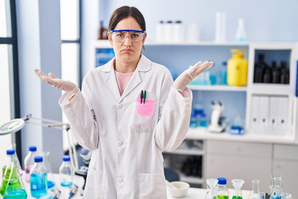 Young brunette woman working at scientist laboratory shouting and screaming loud to side with hand on mouth. communication concept.  - Photo, Image