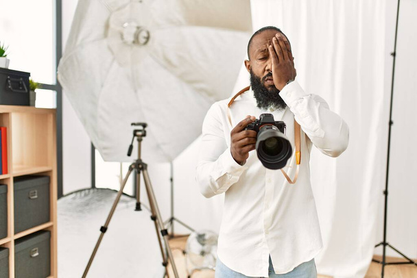 Afrikanisch-amerikanischer Fotograf Mann arbeitet im Fotostudio gähnende Müdigkeit bedeckt das halbe Gesicht, Augen und Mund mit der Hand. Gesicht schmerzt vor Schmerzen.  - Foto, Bild