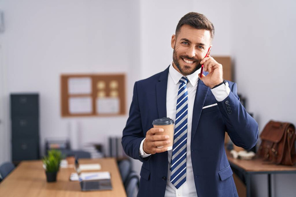 Junger hispanischer Geschäftsmann, der im Büro auf dem Smartphone Kaffee trinkt - Foto, Bild