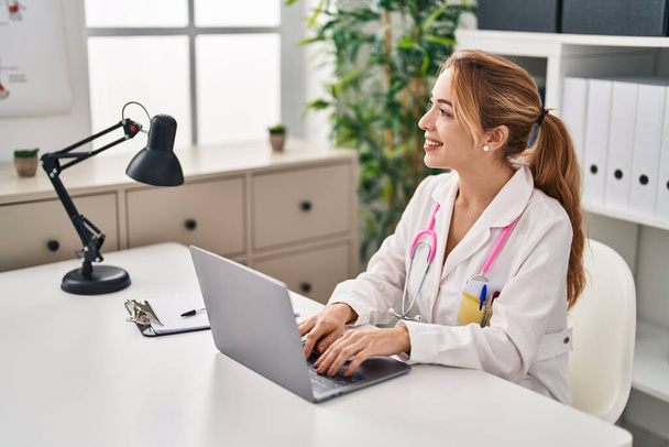 Orvosi egyenruhát viselő fiatal nő laptoppal dolgozik a klinikán - Fotó, kép