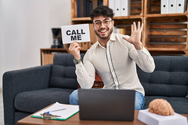 Hispanic man with beard working at therapy office holding call me sign celebrating victory with happy smile and winner expression with raised hands  - Photo, Image