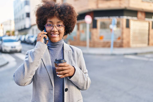 African american woman executive talking on smartphone drinking coffee at street - Photo, image