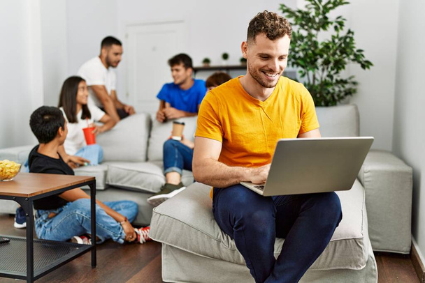 Gruppo di giovani amici sorridenti felici seduti sul divano. Uomo che utilizza computer portatile a casa. - Foto, immagini