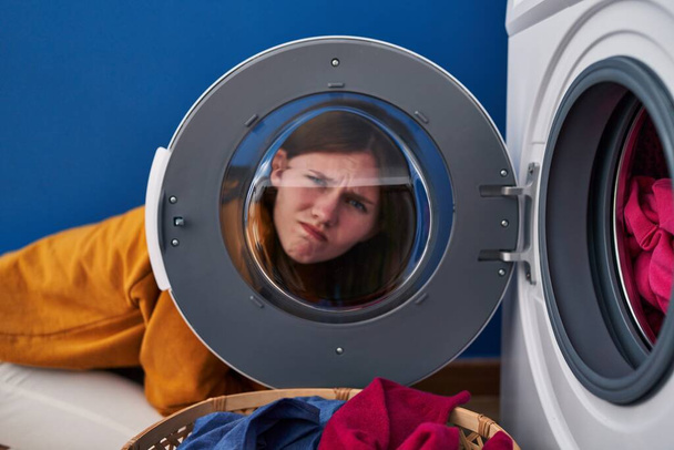 Jeune femme brune regardant à travers la fenêtre de la machine à laver sceptique et nerveux, fronçant les sourcils bouleversés en raison de problèmes. personne négative.  - Photo, image