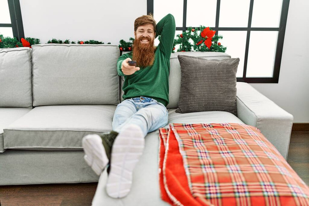 Jeune rousse homme regarder un film assis par décor de Noël à la maison - Photo, image