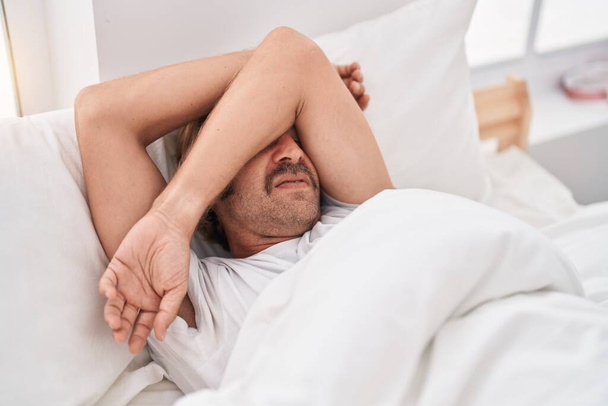 Jonge blonde man gestrest liggend op bed in de slaapkamer - Foto, afbeelding