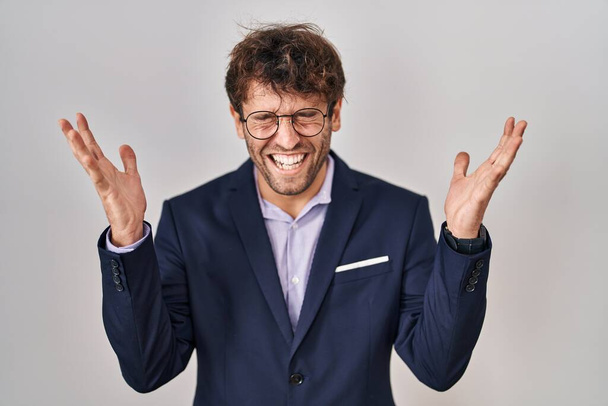Homme d'affaires hispanique portant des lunettes célébrant fou et fou de succès avec les bras levés et les yeux fermés hurlant excité. concept gagnant  - Photo, image
