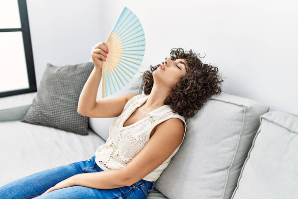 Молодая женщина с Ближнего Востока отчаянно использует ручной вентилятор дома - Фото, изображение
