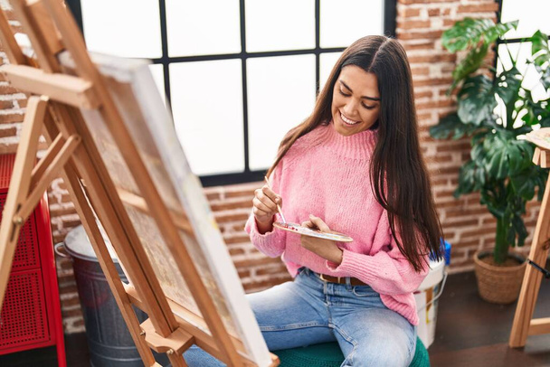 Молода іспаномовна жінка посміхається впевнено малює в художній студії
 - Фото, зображення