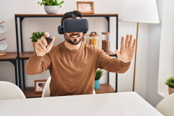 Joven hispano jugando videojuegos usando gafas de realidad virtual en casa - Foto, Imagen