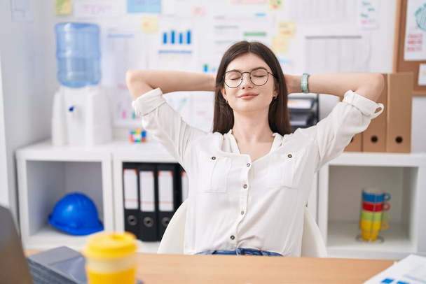 Jonge blanke vrouw zakenman ontspannen met handen op het hoofd op kantoor - Foto, afbeelding