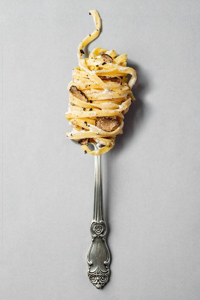 Homemade spaghetti pasta with truffle mushroom slices and creamy sauce is wound on a vintage fork and lies on a gray background. - Foto, afbeelding