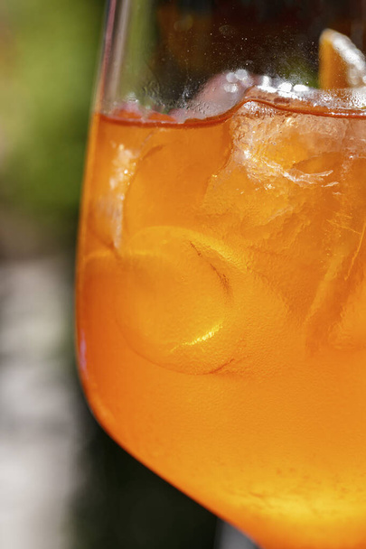 Classic Aperol Spritz cocktail. The cocktail is poured into a glass on a high stem and is held by a woman's hand. Green plants can be seen in the background. - Valokuva, kuva