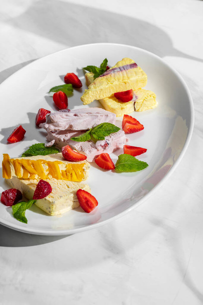Assorted cherry, melon and peach ice cream with strawberries and mint. Ice cream lies on a light ceramic plate on a marble surface. Nearby is a glass of cocktail. - Foto, imagen