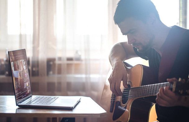 A man learning to play acoustic guitar, watching video lesson on laptop, concept of online learning and self-study. - Φωτογραφία, εικόνα