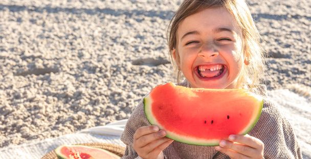Close-up, funny little girl appetizingly eats watermelon on the sea beach. - Fotó, kép