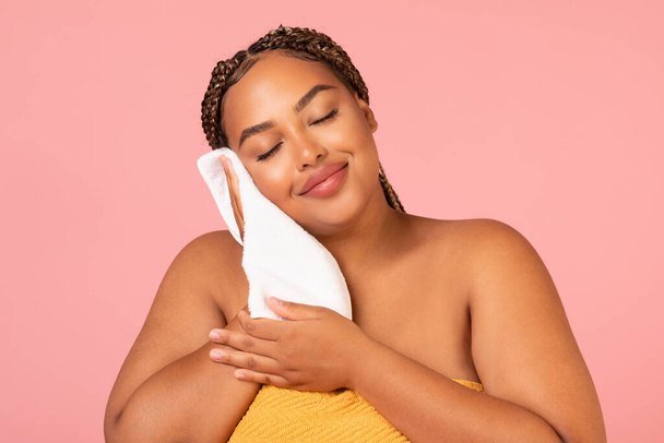 Pretty Overweight Black Lady Drying Face With Soft White Towel Enjoying Facial Skincare Routine Posing Standing Over Pink Background In Studio. Skin Care And Pampering Concept - Foto, afbeelding