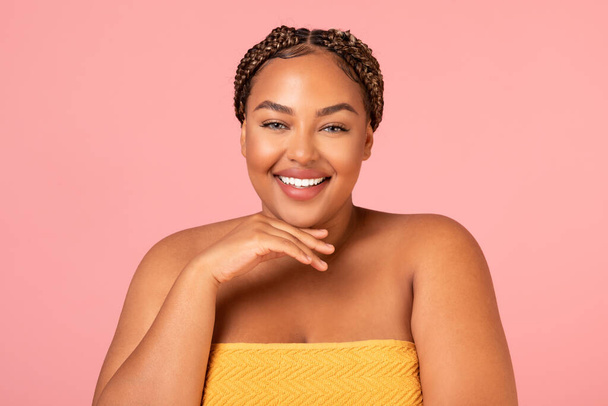 Portrait Of Pretty Obese Black Female Wrapped In Towel Smiling To Camera Posing Holding Hand Near Face Over Pink Studio Background. Beauty Routine And Wellness Concept - Foto, Imagem