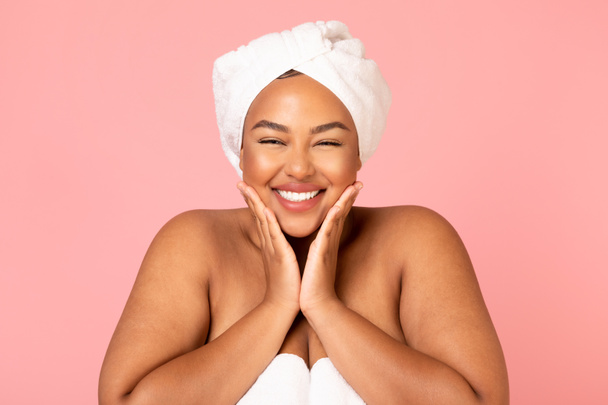 Facial Skincare. Happy Overweight African American Woman Touching Face With Both Hands Smiling To Camera Posing Wrapped In Towel On Pink Studio Background. Beauty Routine And Pampering - Photo, Image