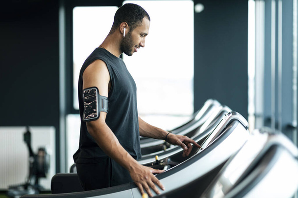 Sporty Muscular African American Guy Training On Treadmill At Gym, Motivated Young Black Man Choosing Running Mode, Male Athlete Touching Control Panel And Smiling, Ready For Workout, Copy Space - Zdjęcie, obraz