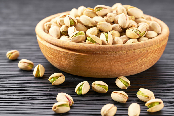 Pistachios in wooden bowl on black table. Organic pistachios, healthy food. Bowl with pistachios on a wooden table. - Foto, immagini