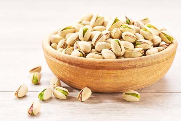Pistachios in wooden bowl on white table, close-up. Bowl with pistachios on a wooden table. - Foto, Imagem