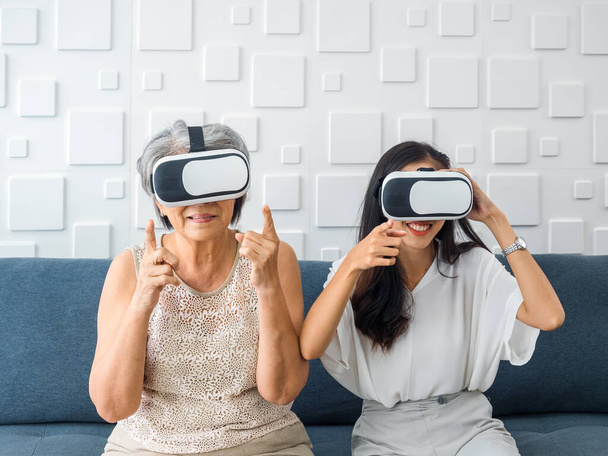 Asian old senior woman, mother and happy young daughter, female wearing VR glasses, enjoy 3d game online together in white room. Mom and daughter with reality virtual technology lifestyle concept. - Fotó, kép
