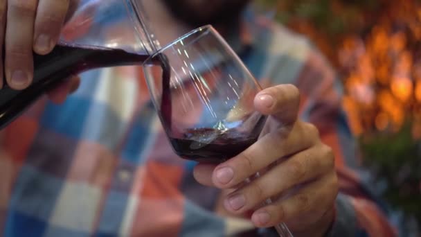 Férfi kéz közelről Livacette-ben egy pohár kancsó vörösborban. A szakállas férfi nem fókuszál, az emberek isznak a bárban vagy az étteremben. Borkóstoló. Mintavevő. - Felvétel, videó