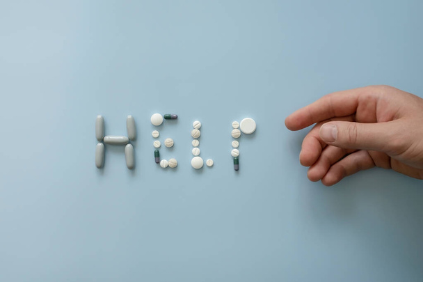 Word HELP je lemován různými pilulky vedle oslabené ruky, na modrém pozadí. Lékařský koncept, problémy deprese, stresu a léků. Horní pohled. Detailní záběr.  - Fotografie, Obrázek