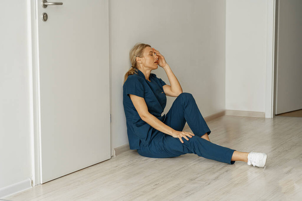 Tired nurse sits on floor in the lobby of medicine clinic after a hard dutty. High quality photo - Foto, imagen