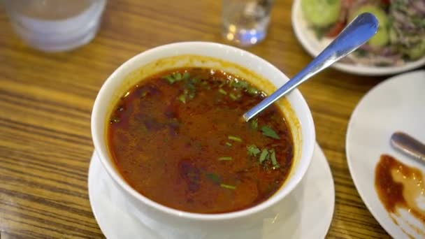 伝統的なグルジアのスープ木製のテーブルの上にボウルにハルチョ。国民食。木製のテーブルの上にコリアンダーと野菜とスープカルチョ.牛肉、米、ニンニク、トケマリソースとスパイシーなスープのボウル, - 映像、動画
