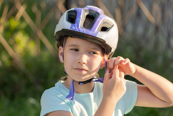 School age biker, child taking off or putting on a protective biking helmet, young cyclist portrait, face closeup, girl fastening her helmet. Blurred background, children and biking, cycling, sports - Fotoğraf, Görsel